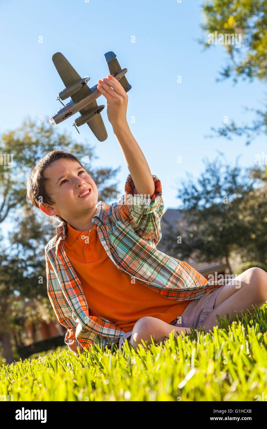 A young boy sitting on grass outside playing with a toy model airplane ...
