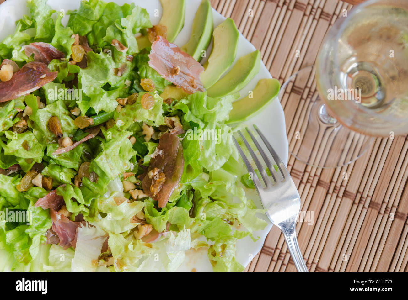 Green mix salad plate with avocado, prosciutto, raisins and pecans over bamboo mat Stock Photo