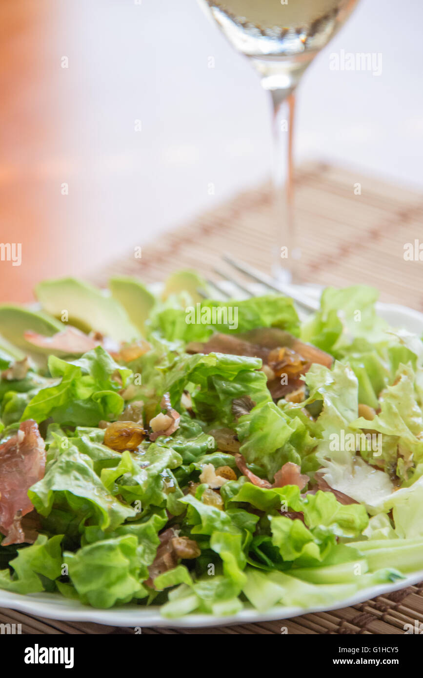 Green mix salad plate with avocado, prosciutto, raisins and pecans over bamboo mat Stock Photo