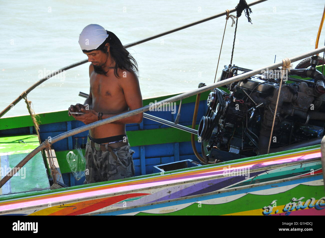 Long tailed boat Thailand close up of crew with mobile phone Stock Photo