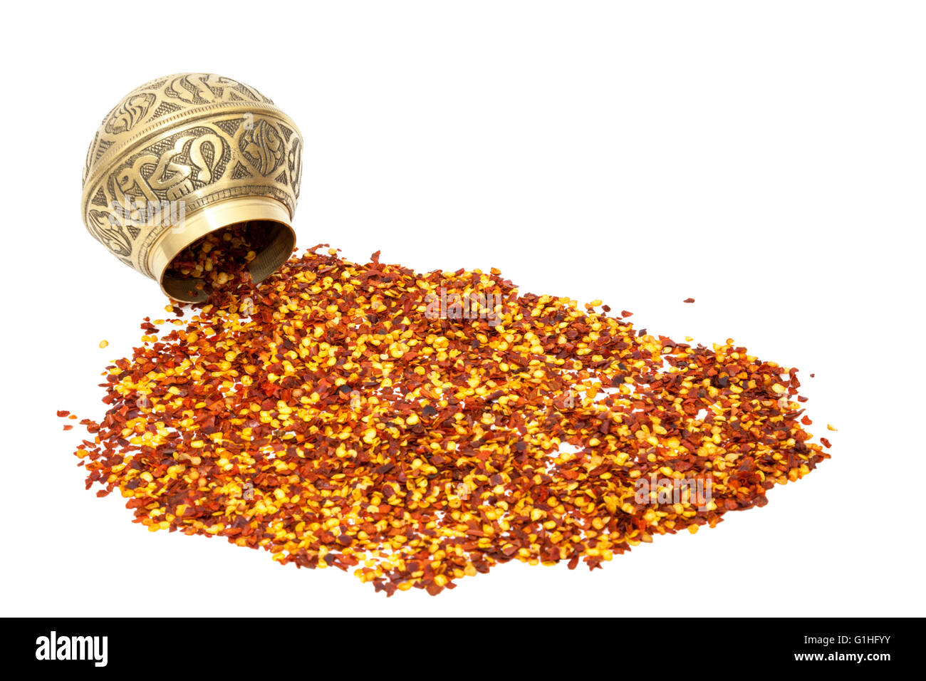 Chilli flakes spilling from a metal spice bowl isolated on a white background Stock Photo