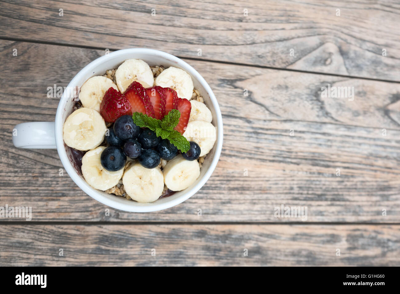 Acai bowl with fresh fruit strawberry, blueberry, banana and peppermint leaves on top on the wooden table. Stock Photo