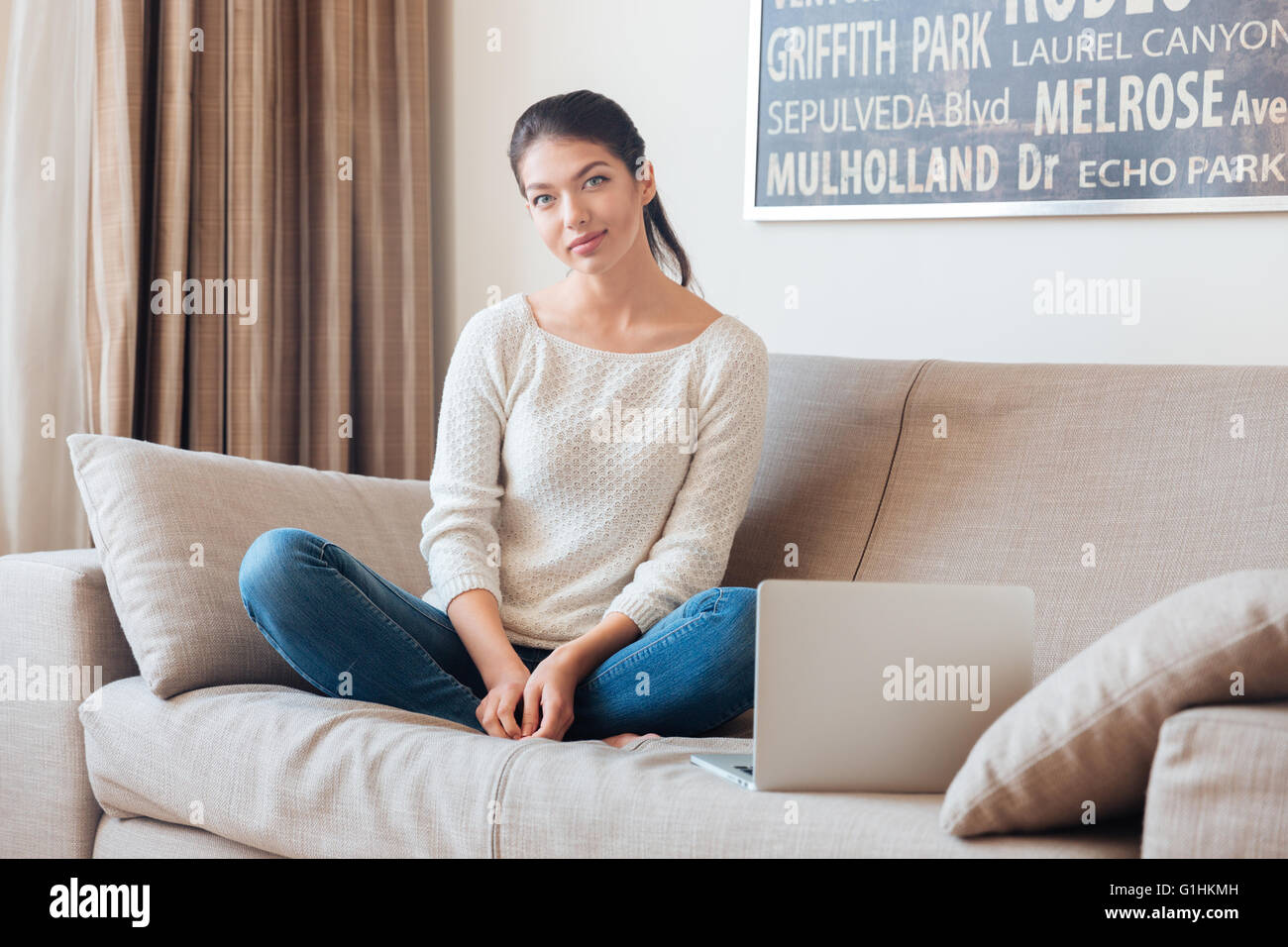 Happy woman sitting on the sofa with laptop and looking at camera Stock ...