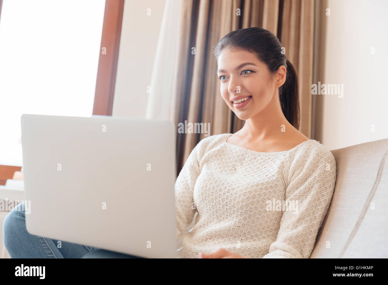 Happy young woman sitting on the sofa with laptop computer at home ...