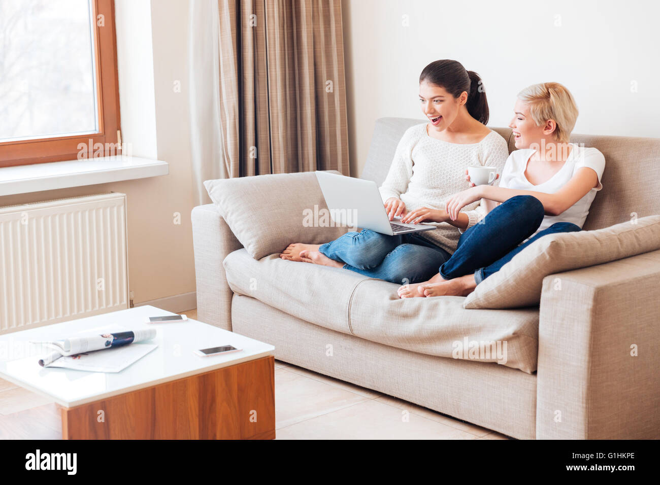 Two cheerful women using laptop computer on the sofa at home Stock ...