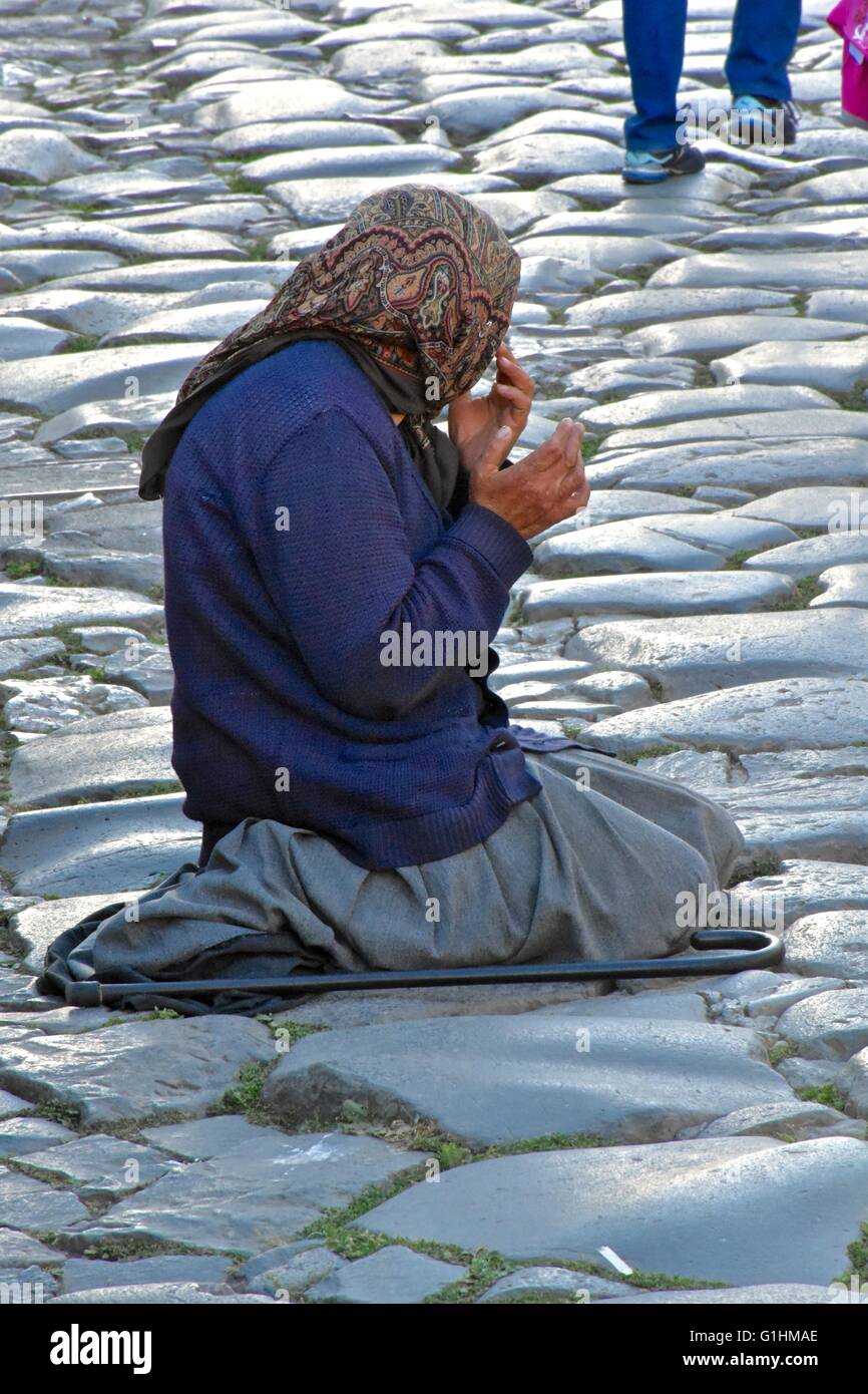 A homeless woman on the streets of Rome kneeling on the ground while praying and asking for money Stock Photo
