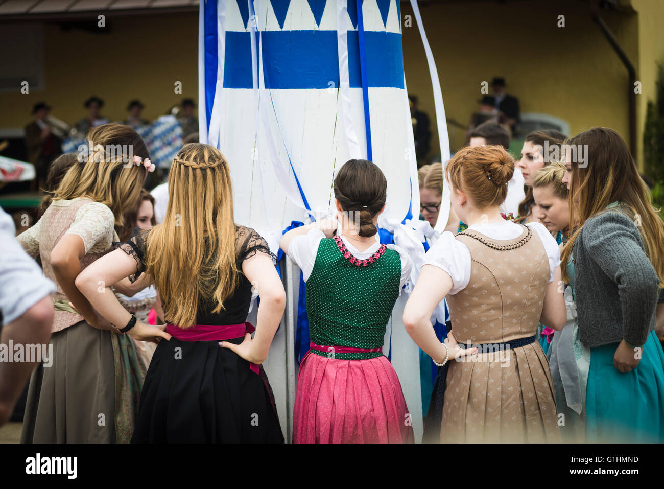 Women and men in local costumes dancing a traditional bavarian folk dance  knotting blue and white ribbons to the maypole Stock Photo