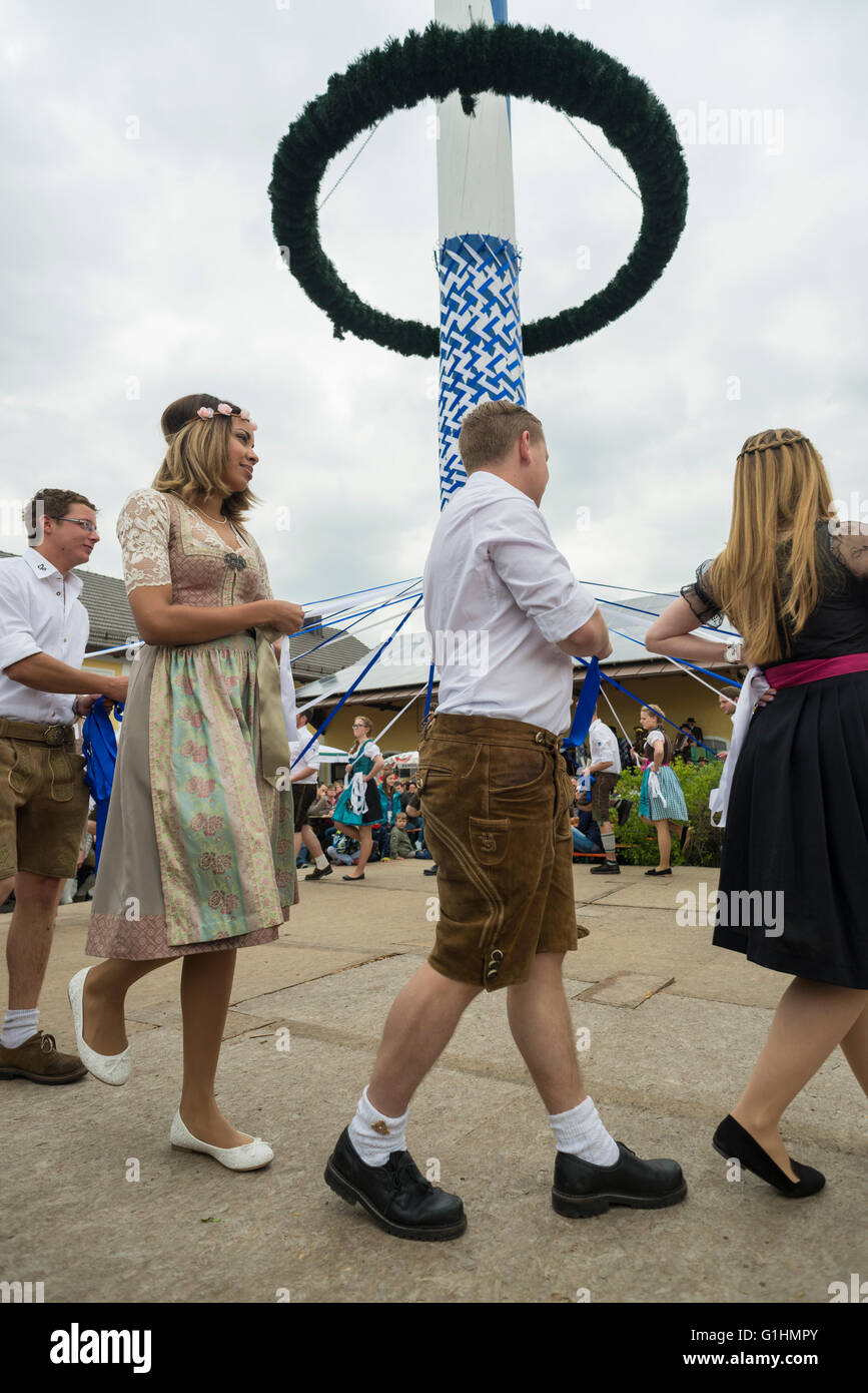 Women and men in local dirndl dressen an lederhosen dancing a traditional Bavarian folk dance  around the maypole holding blue and white ribbons Stock Photo