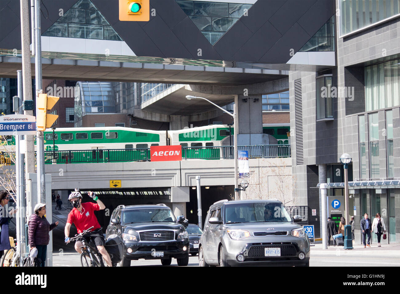 GO train traveling over lower Simcoe St. at Bremmer Blvd with commuters in cars, bike and walking Stock Photo