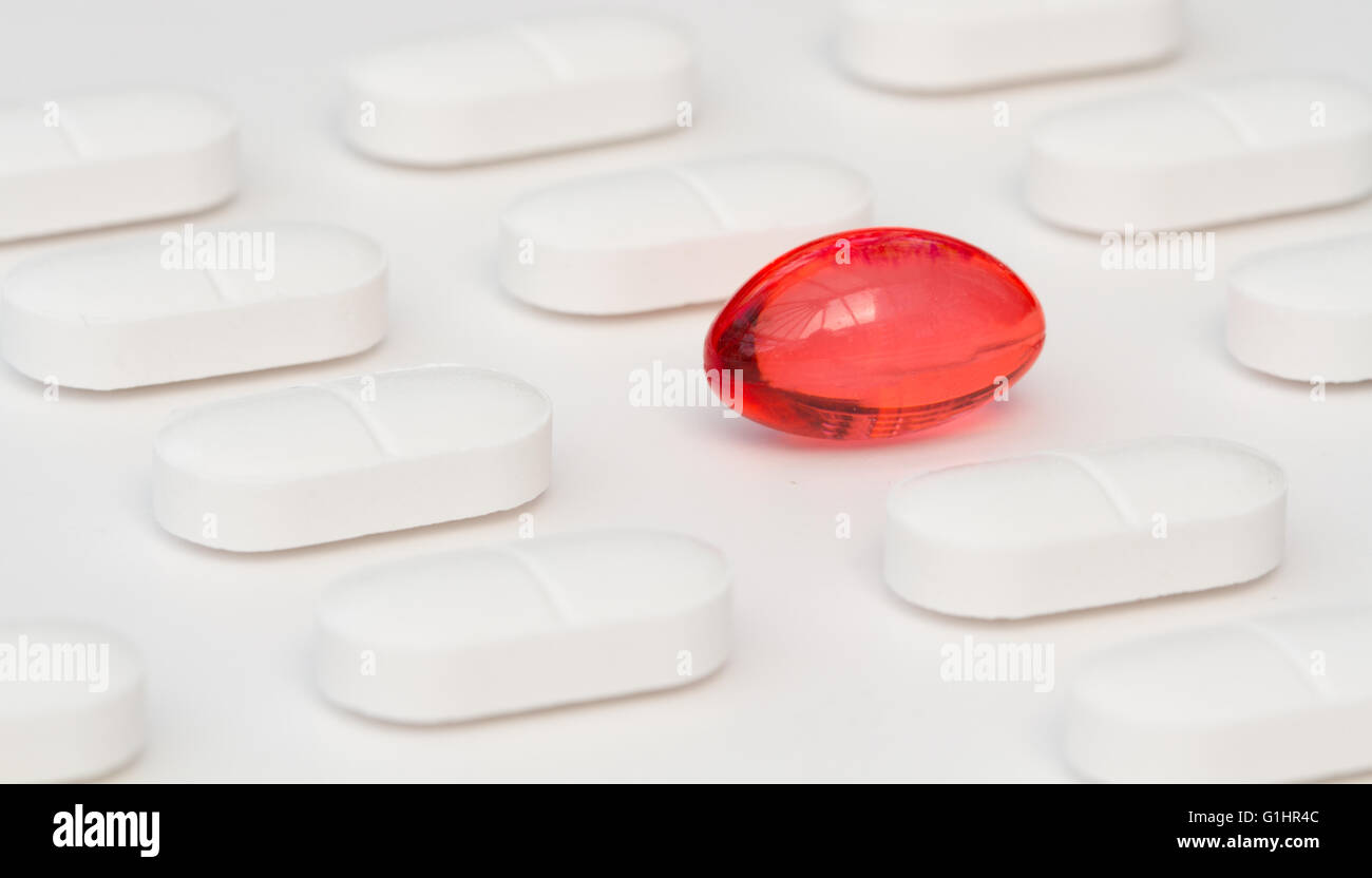 Rows of white painkilling tablets on a white background with a single, red medicinal capsule standing out from the rest. Stock Photo