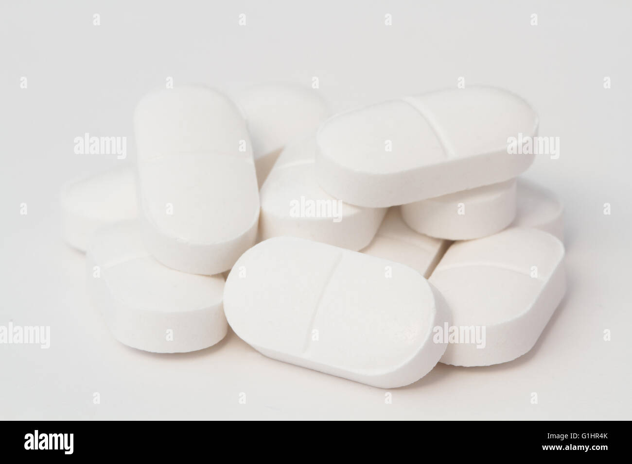 A small pile of white painkilling tablets or paracetamol with two halves on an isolated white background. Stock Photo