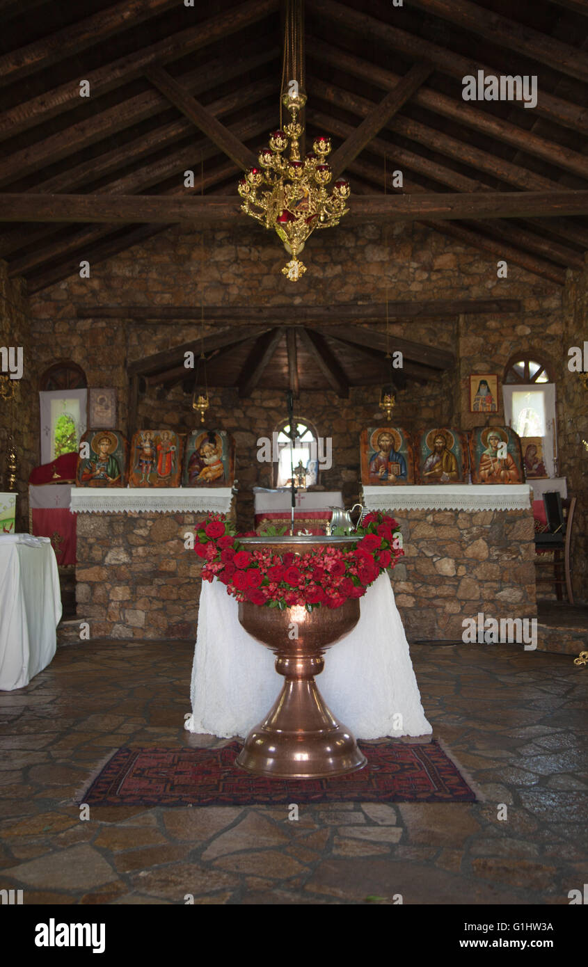 Christian church interior decorated for baptism with baptismal font red flowers white linen