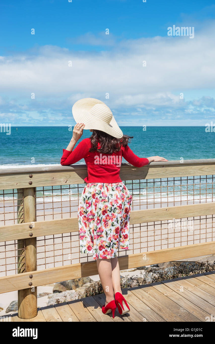 beautiful woman in red standing and looking to the sea Stock Photo