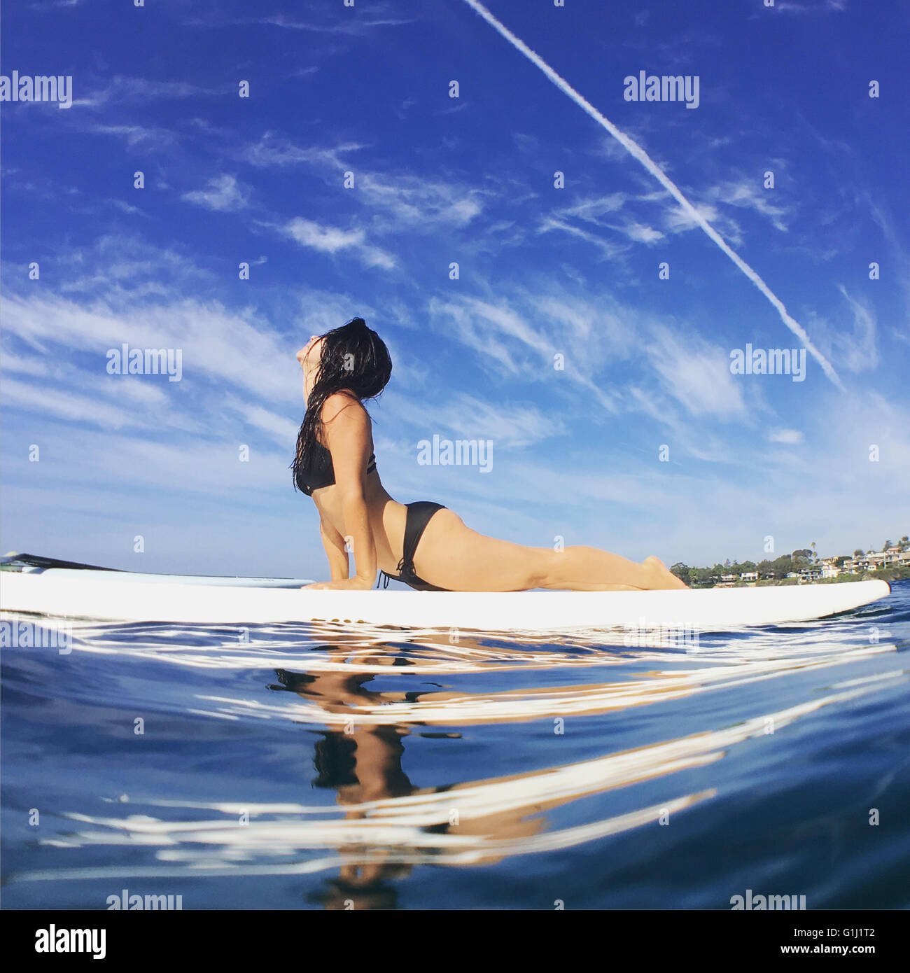 Woman doing yoga (cobra pose) on surfboard in ocean Stock Photo