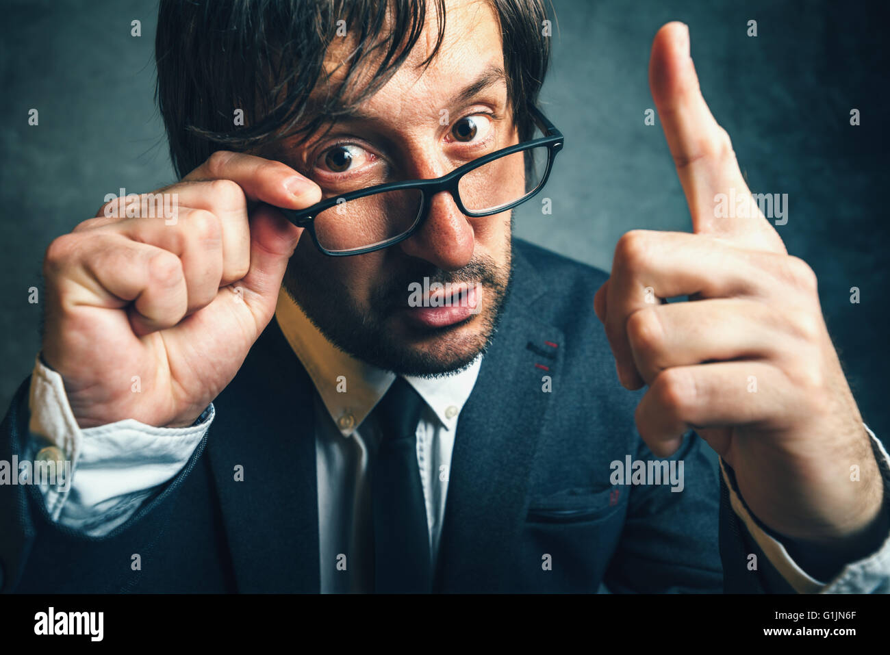 Angry tax inspector looking serious and determined, aggressive finger threatening adult businessperson with glasses Stock Photo