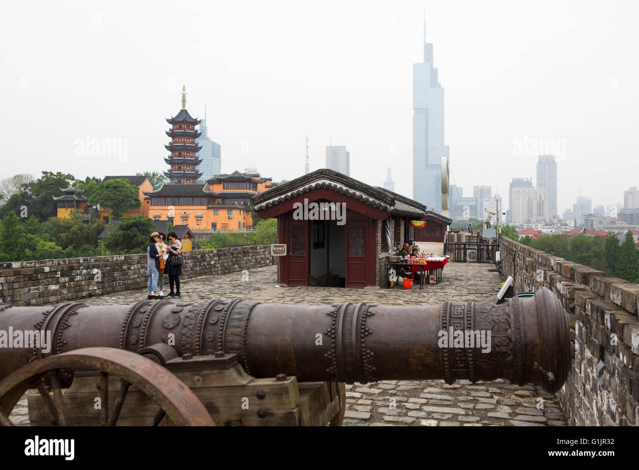 Historical city wall of Nanjing with a cannon in front, Jiming temple and skyline of Nanjing with towers in the hazy background Stock Photo