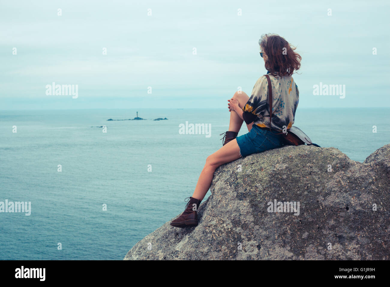 A young woman is sitting on a rock by the sea Stock Photo - Alamy
