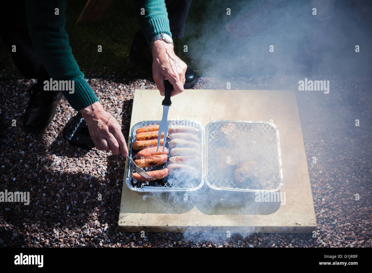 Closeup on the hands of an elderly man as he is attending to a barbecue outdoors at night Stock Photo