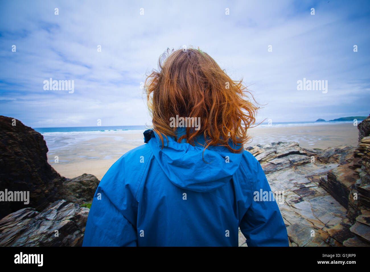 A young woman is standing on the coast and is looking at the sea Stock ...