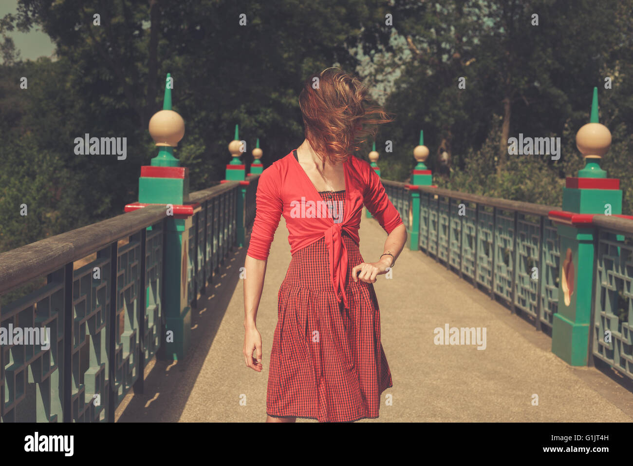 A young woman wearing a red dress is standing on a bridge in a park Stock Photo