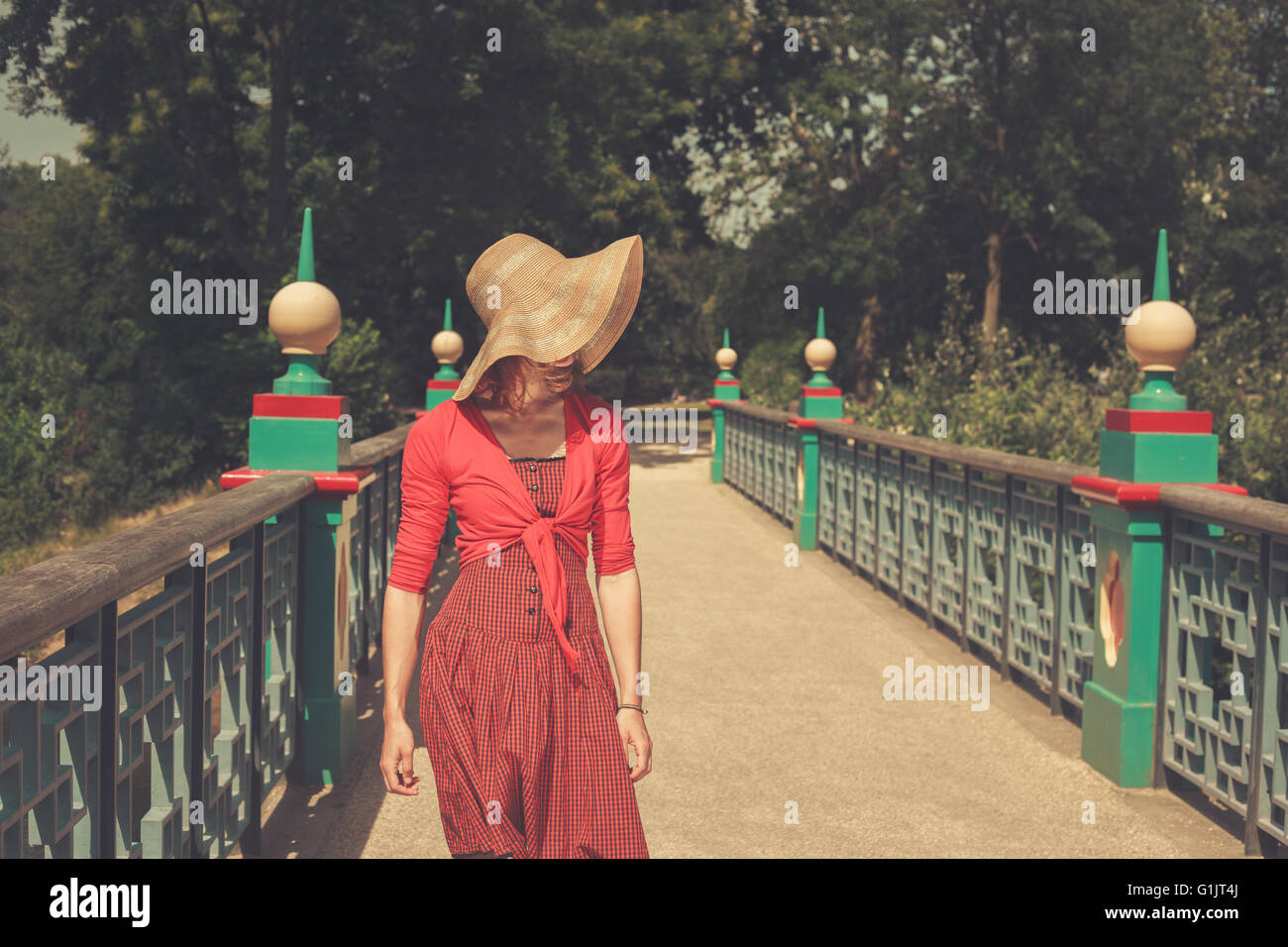 A young woman wearing a red dress is standing on a bridge in a park ...