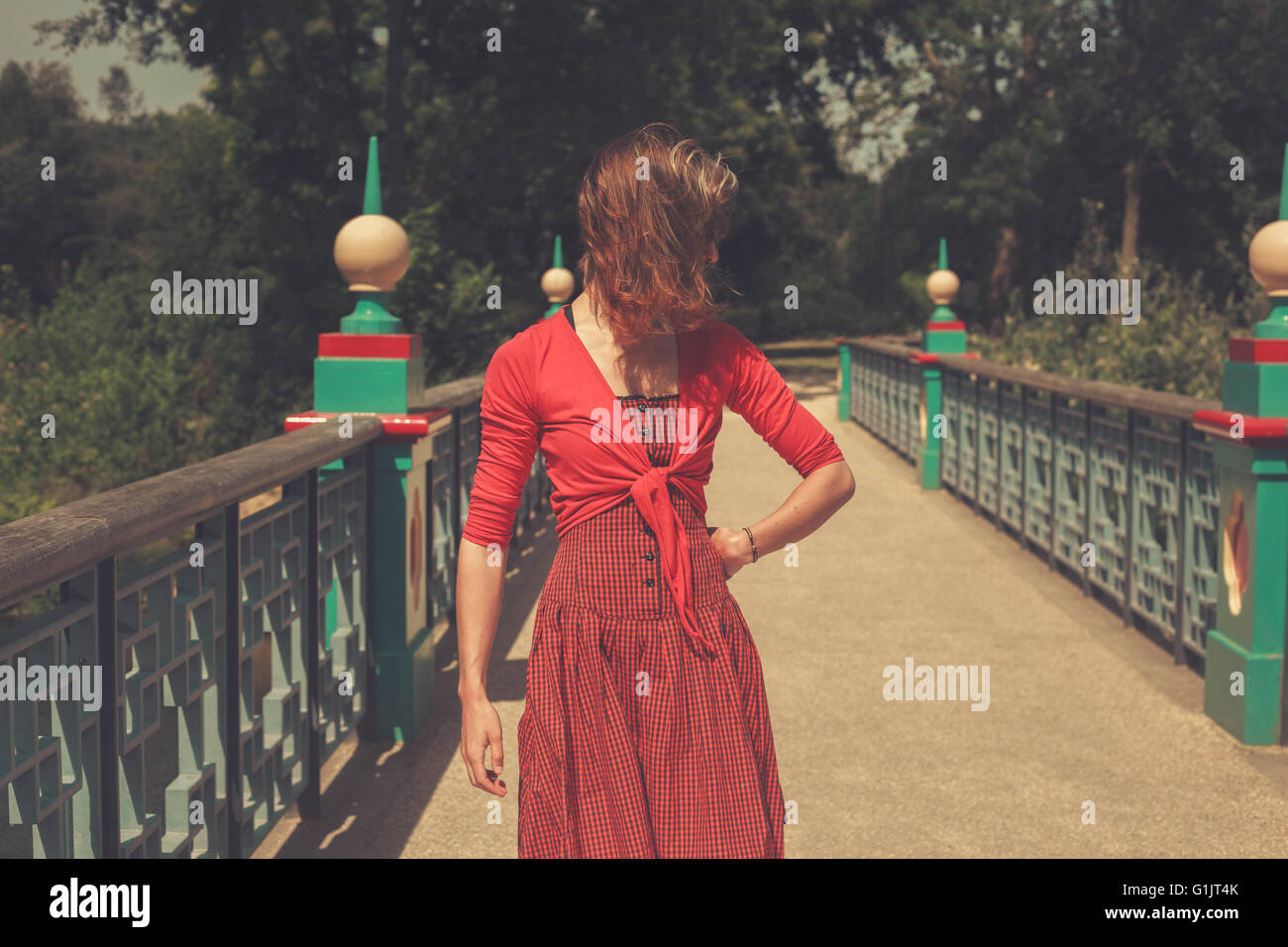 A young woman wearing a red dress is standing on a bridge in a park Stock Photo