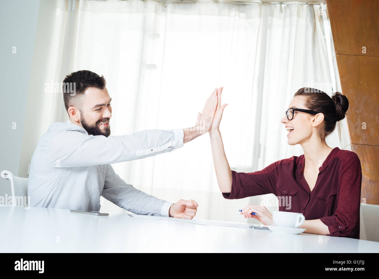 Two happy successful young businesspeople sitting and giving high five ...