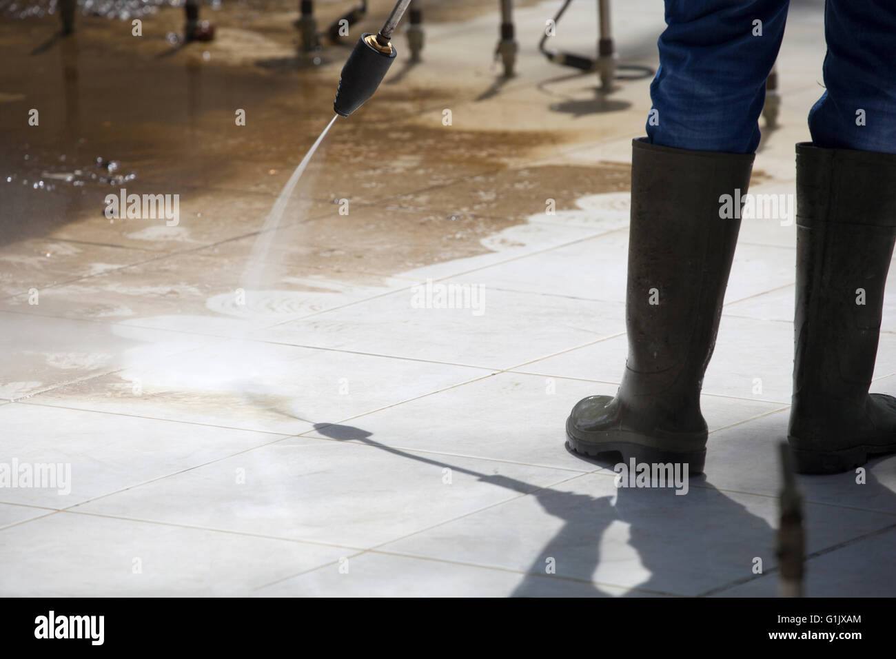 Worker in rubber boots, cleaning an outdoor fountain by pressure washer in a sunny day. Stock Photo