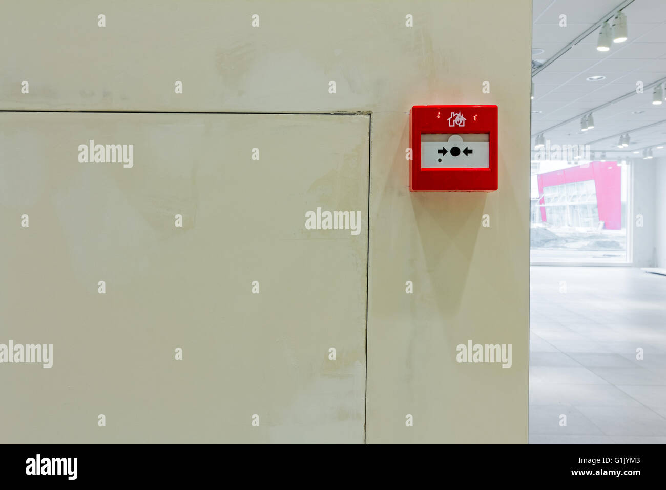 Red fire alarm panel box is on the wall, to smash glass and press
