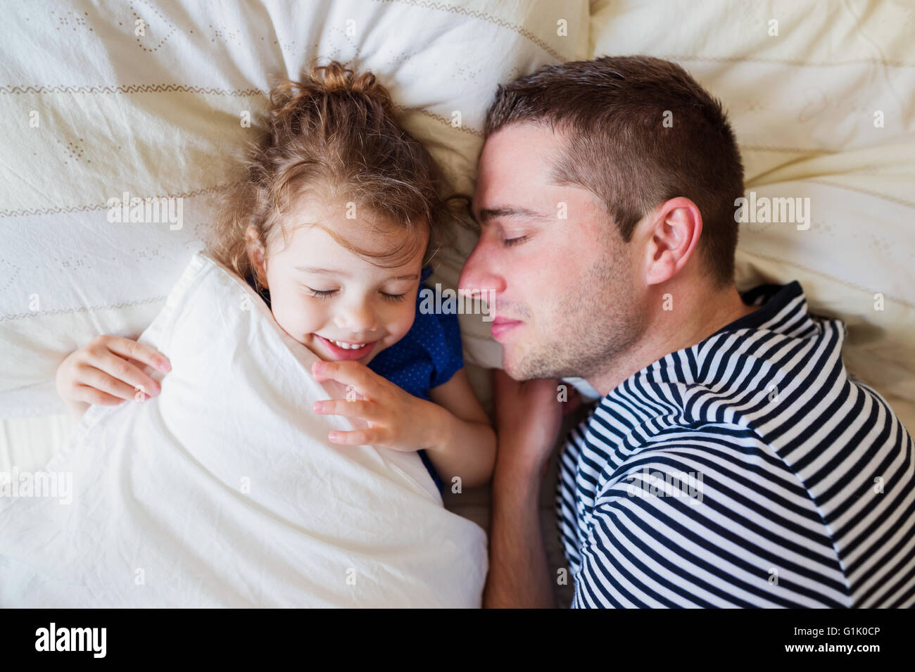 Father and daughter lying in parents bed, sleeping, smiling Stock Photo
