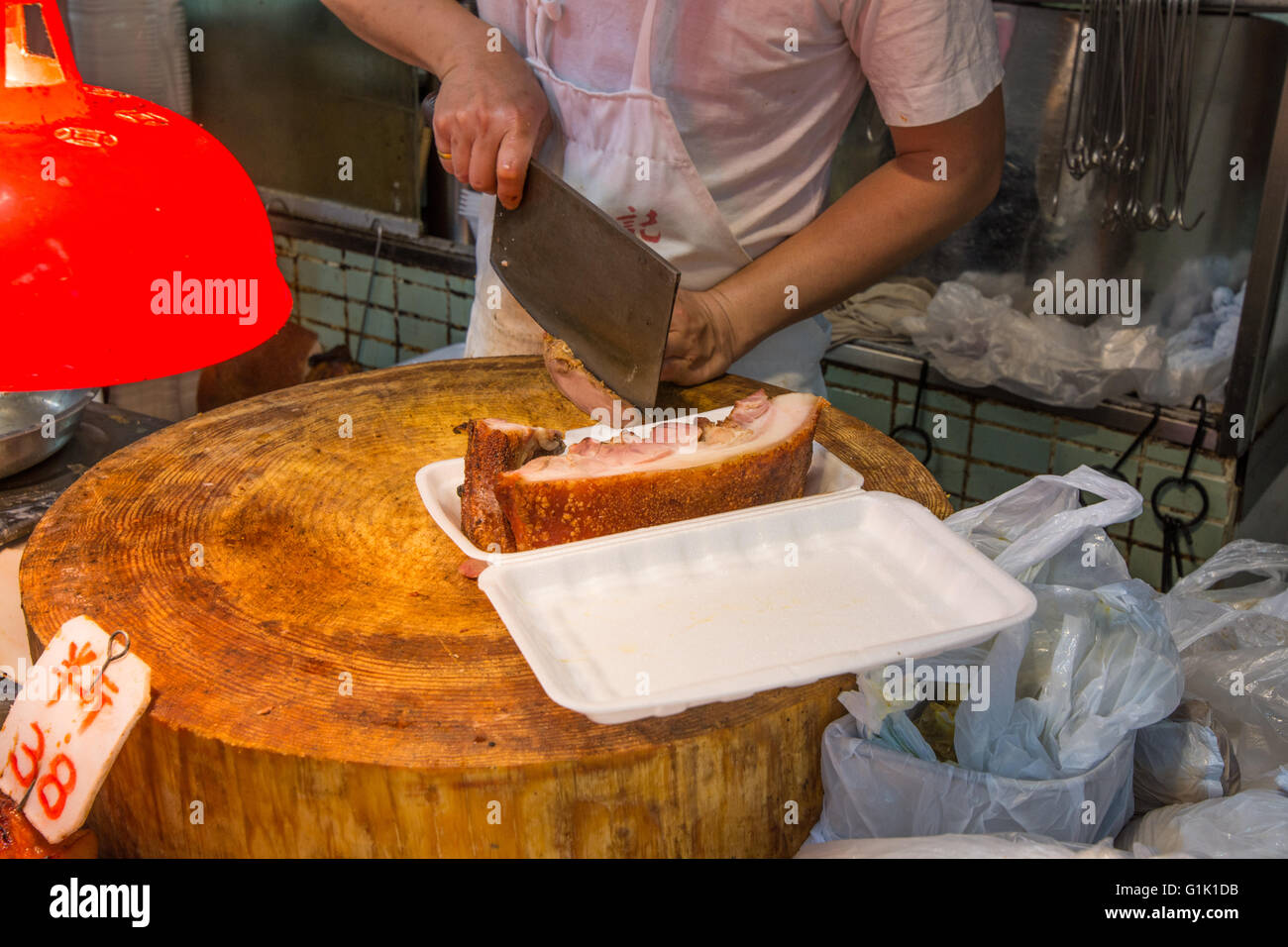 Person cutting crispy pork on chopping board at Chinese food stall Stock Photo