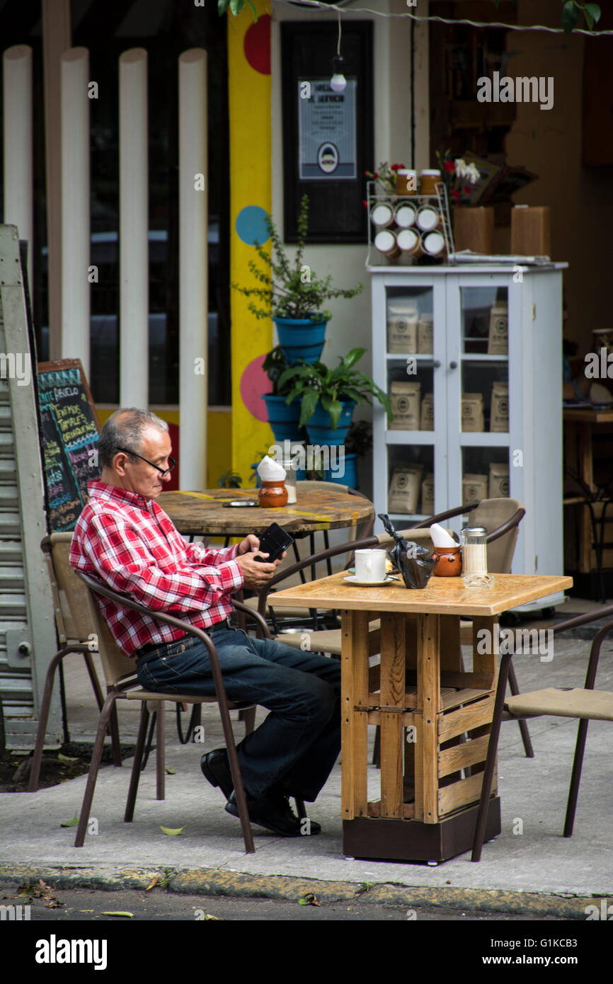 Old man texting and drinking coffee alone on a sidewalk table. Mexico. Stock Photo
