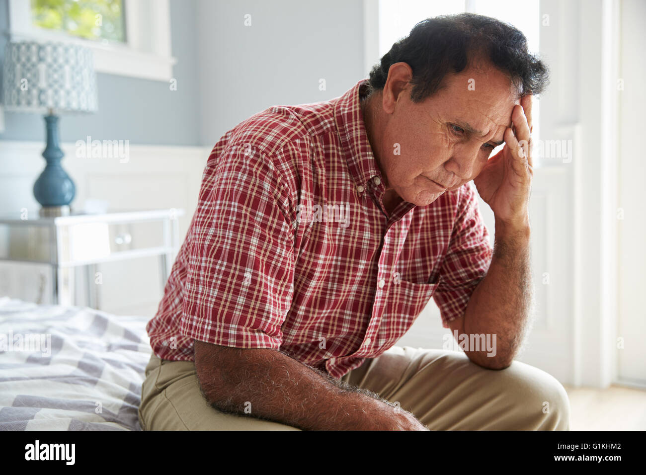 Senior Hispanic Man Sitting On Bed Suffering With Depression Stock Photo