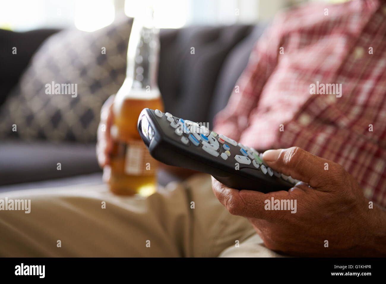 Man Sitting On Sofa Holding TV Remote And Bottle Of Beer Stock Photo