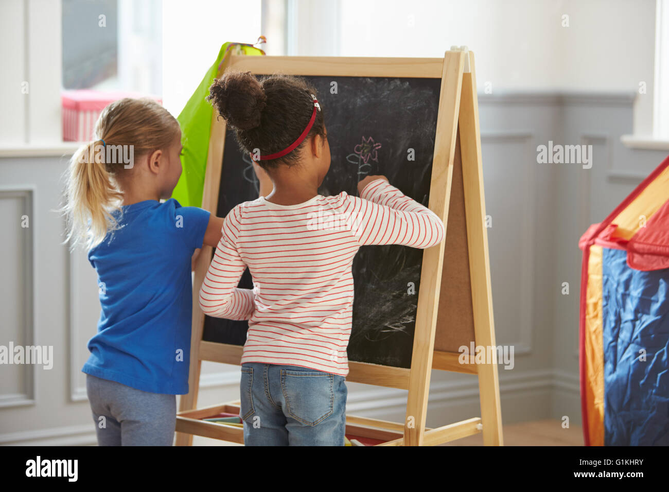 Two Girls Drawing Picture On Blackboard At Home Stock Photo