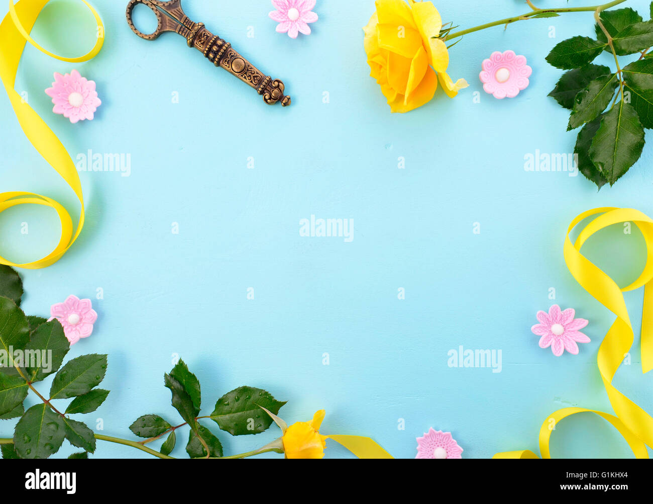 Summertime background with decorated borders of yellow roses, pink candy and yellow ribbon on pale blue wood table, with copy sp Stock Photo