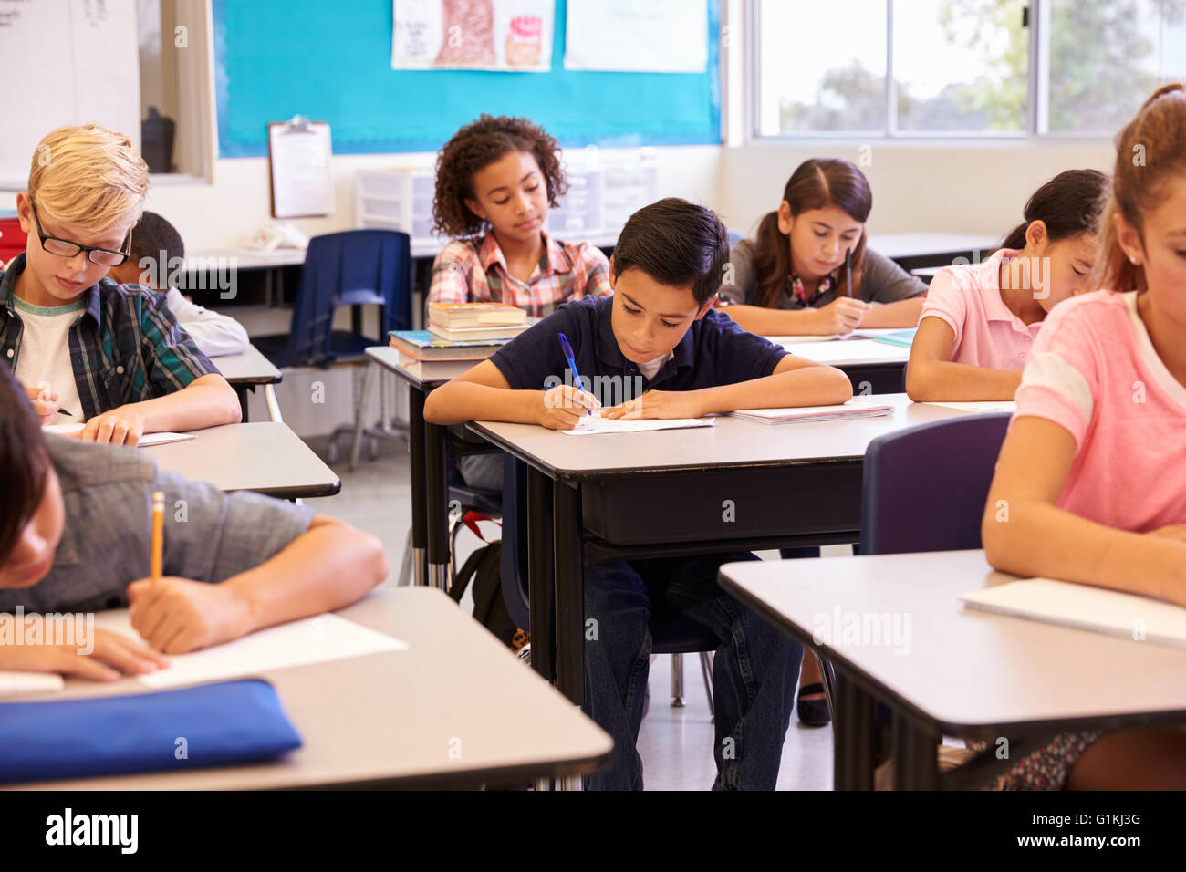 Elementary School Kids Working At Their Desks In A Classroom Stock