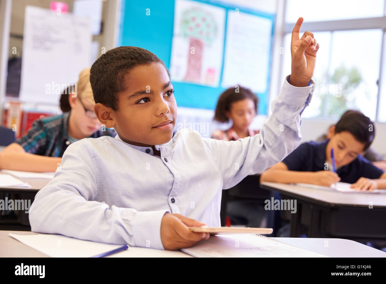 Boy with tablet raising his hand in elementary school class Stock Photo ...