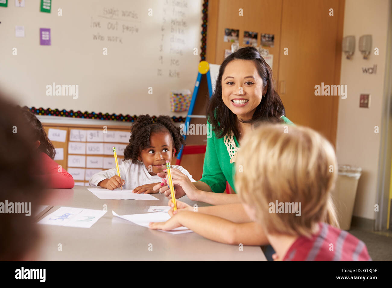 Teacher sitting with kids in elementary school lesson Stock Photo - Alamy
