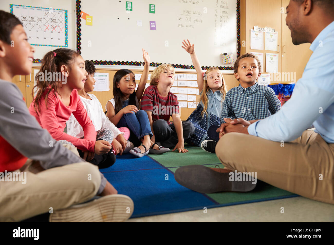 Elementary school kids and teacher sit cross legged on floor Stock