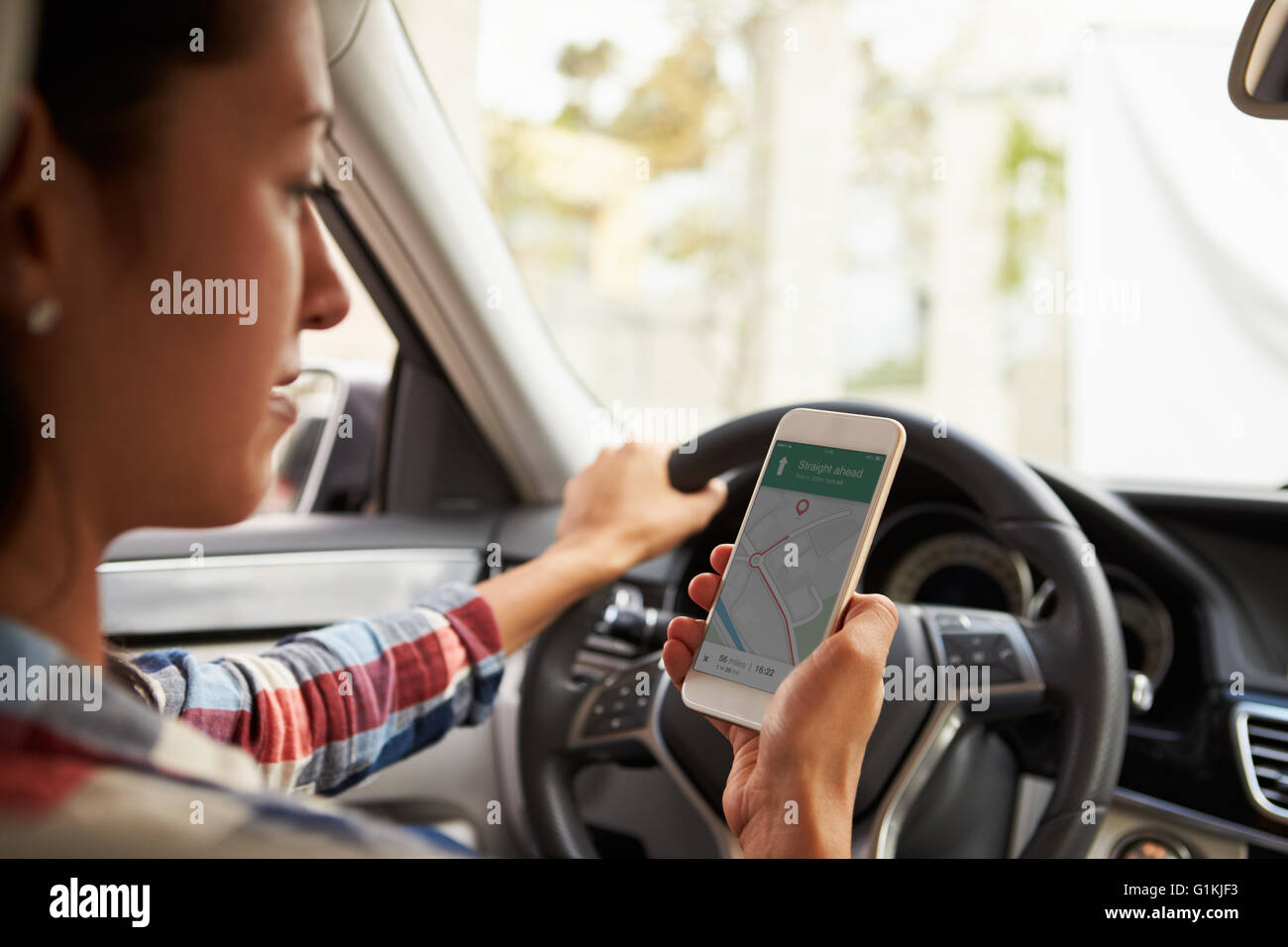 In car view of Hispanic female driver looking at Maps App on her phone Stock Photo
