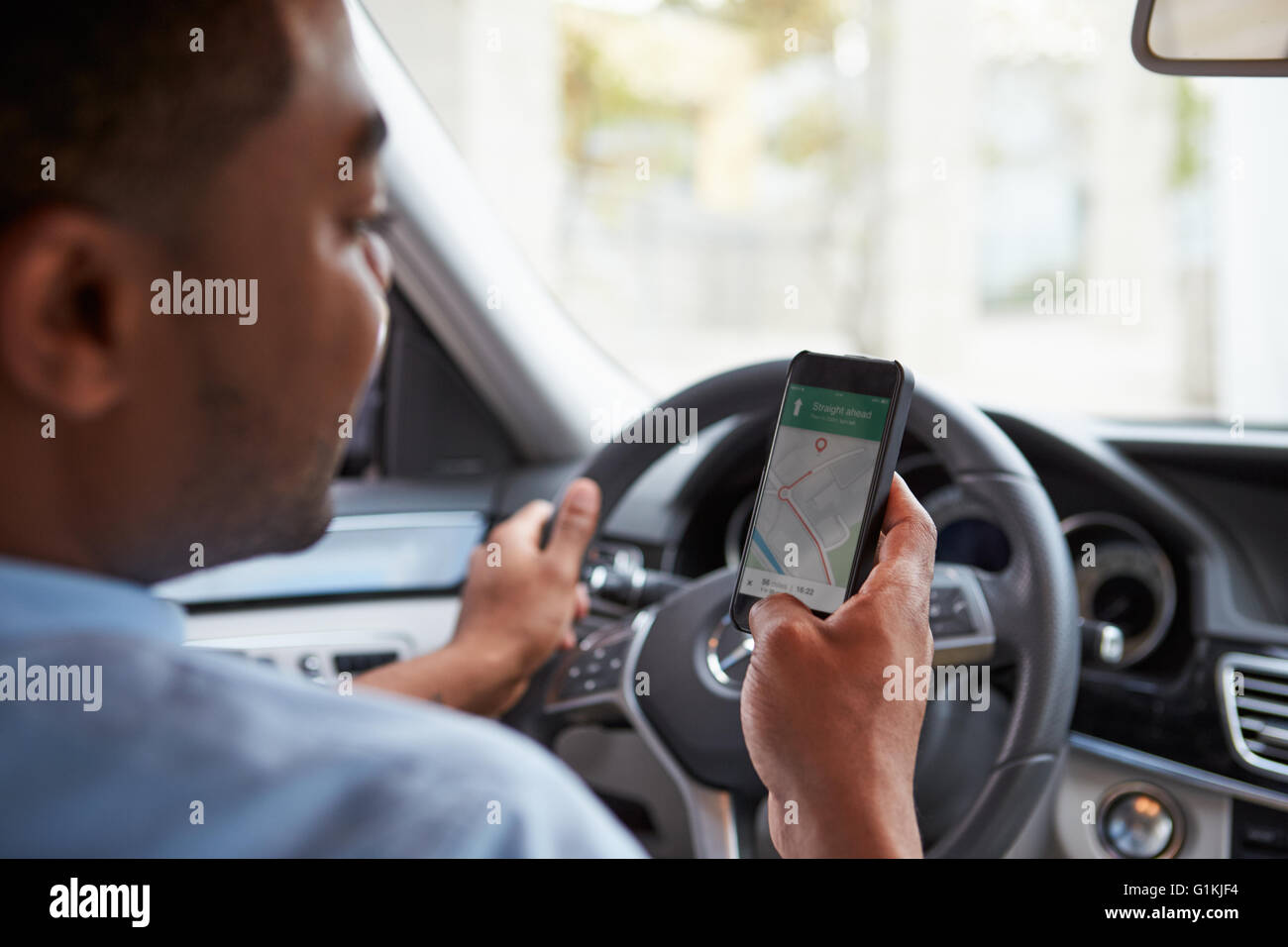 In car view of young male African American looking at maps app on his phone Stock Photo