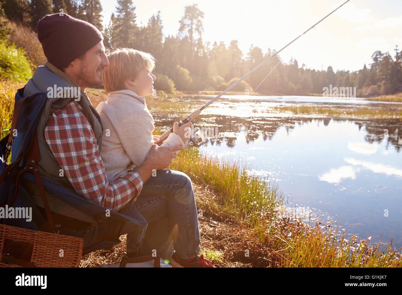 Father teaching son to fish sitting at lakeside Stock Photo