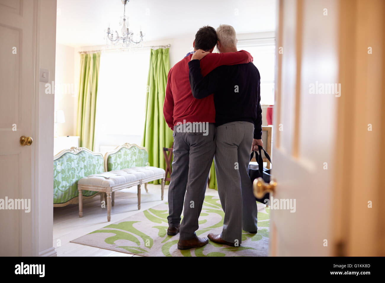 Male couple with arms around each other arrive in hotel room Stock Photo