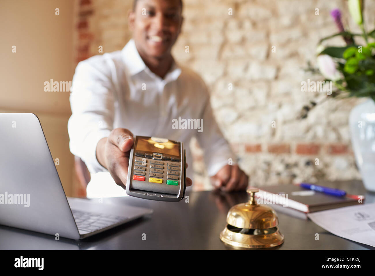 Concierge at hotel reception holds credit card reader to camera Stock Photo
