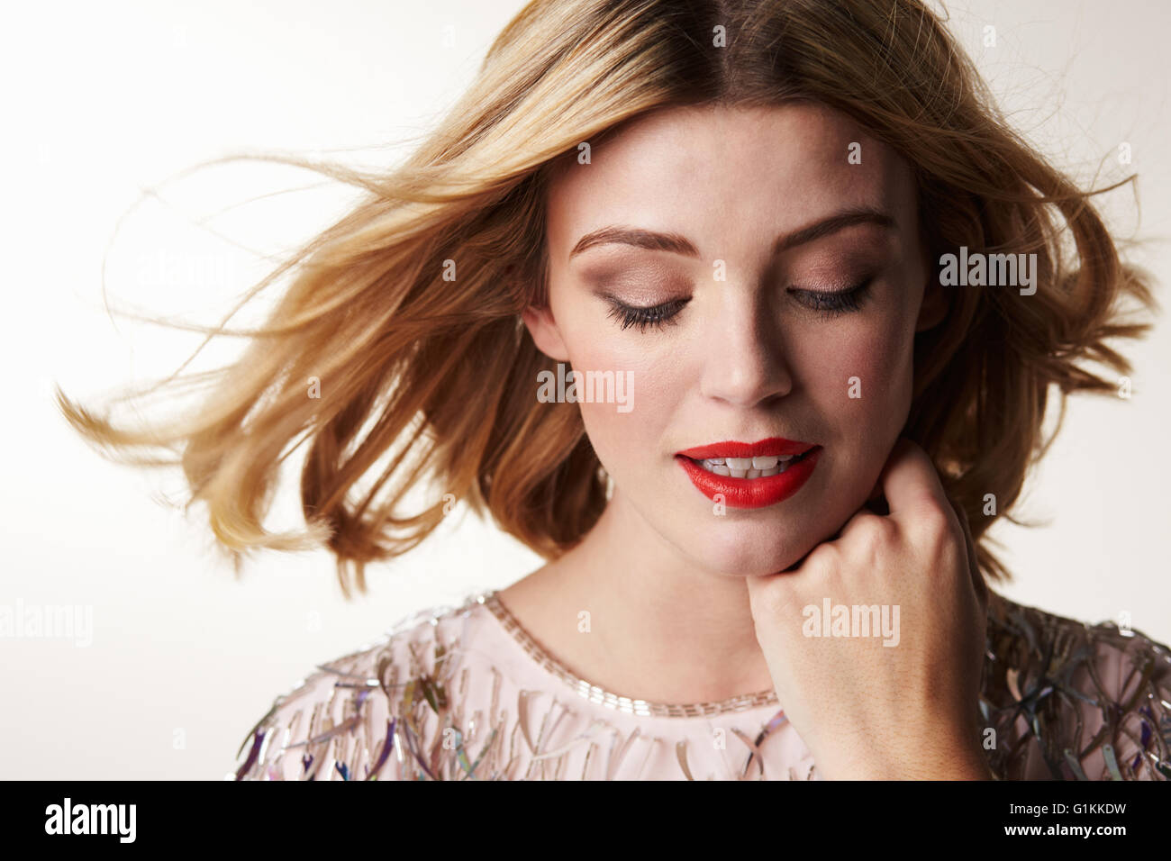 Glamorous blonde woman looking down, chin resting on hand Stock Photo