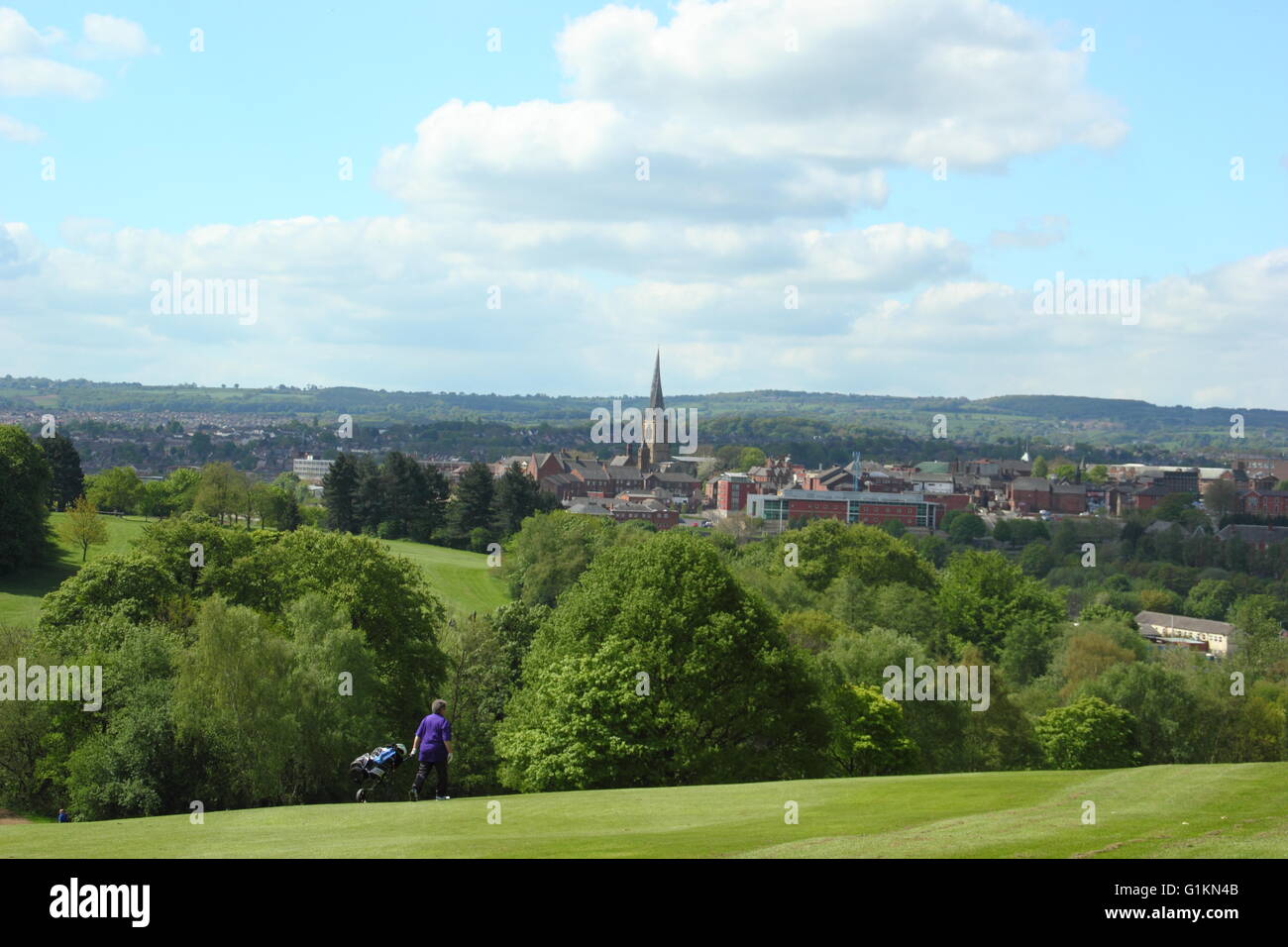 A golfer crosses the green of Tapton Park golf course looking to Chesterfield town centre's twisted spire church & distant hills Stock Photo