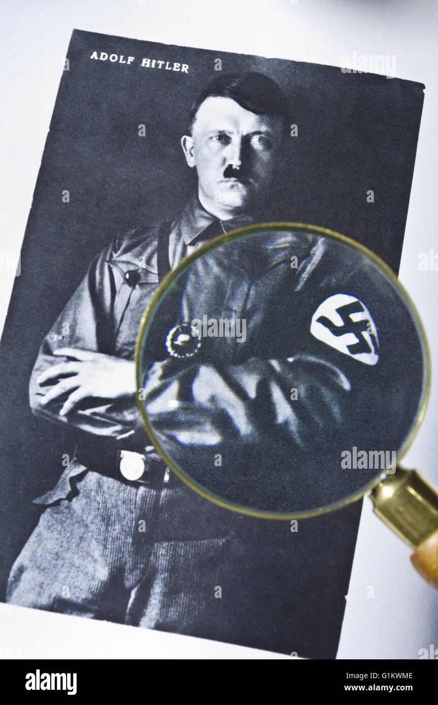 1930's B&W studio posed portrait photograph of Adolf Hitler in uniform with history researchers magnifying glass viewing detail incl. swastika motif Stock Photo
