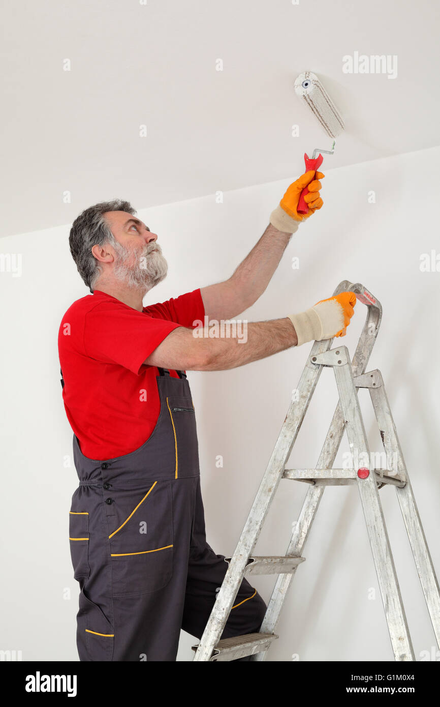 Worker Painting Ceiling With Paint Roller From Ladder Stock Photo