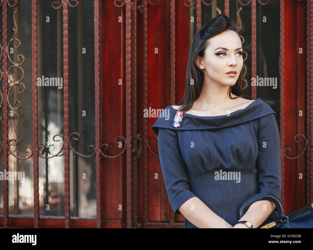 Portrait of a beautiful young woman standing in front of the red door ...
